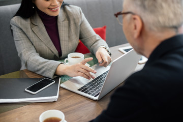 cropped view of smiling businesswoman using laptop and talking with businessman during business meeting