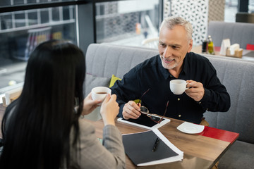 selective focus of smiling businessman holding cup and talking with businesswoman in cafe