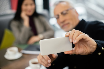 selective focus of businessman taking selfie with businesswoman in cafe