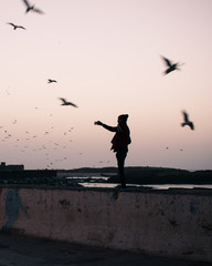 Silueta de una persona haciendo una foto con el móvil al atardecer, rodeada de gaviotas