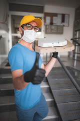 Fototapeta na wymiar Deliveryman with protective medical mask holding pizza box - days of viruses and pandemic, food delivery to your home.