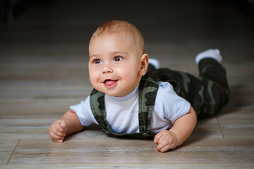 Naklejka premium little boy aged 8 months in overalls, a white shirt and white socks crawling on the floor and smiling