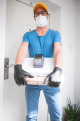 Fototapeta na wymiar Deliveryman with protective medical mask holding pizza box and POS wireless terminal for card paying - days of viruses and pandemic, food delivery to your home and safety hygiene measures.