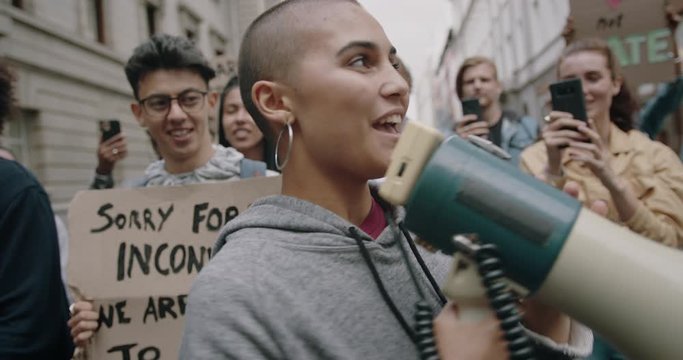 Female activist shouting on a megaphone in a protest march. Youngsters protesting for their civil rights.

