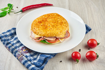 Appetizing sandwich in Italian tortilla focaccio with ham, cheese, onions, tomatoes and lettuce on a white plate on a wooden background. Close up