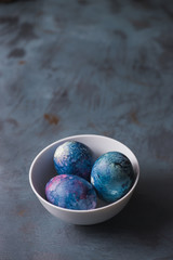 
Easter colored eggs in a white bowl on a textured blue background.