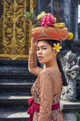 Fototapeta na wymiar Asian girl. Beautiful Balinese women in traditional dress with yellow plumeria frangipani flower makes offering for Gods near the temple. Balinese tradition.