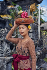 Fototapeta na wymiar Asian girl. Beautiful Balinese women in traditional dress with yellow plumeria frangipani flower makes offering for Gods near the temple. Balinese tradition.