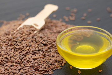 A pile of flax seeds and flax oil in a wooden spoon on a black stone background. dark background Flaxseed concept.