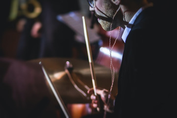 View of drum set kit on a stage during jazz rock show performance, with band performing in the background, drummer point of view