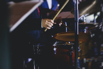 View of drum set kit on a stage during jazz rock show performance, with band performing in the background, drummer point of view