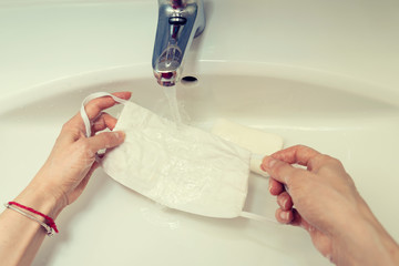 Obraz na płótnie Canvas Female Caucasian hands in laundering handmade protective mask with soap and water on a sink Selective focus