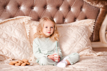 Fototapeta premium Cute baby 3-4 year old drinking milk and eating cookies in bed closeup. Breakfast time. Good morning. Childhood.