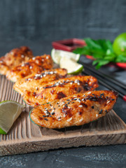 Baked mussels with mozzarella cheese, spices and sesame seeds. On a wooden board. Decorated with lime slices. Close-up. In the background is lime, a bowl of soy sauce, chopsticks. Grey background.
