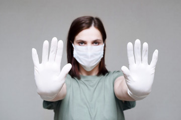 Corona virus. Young woman in a face mask and rubber gloves on a grey background. Protection against infection, virus, dust, keep a distance	
