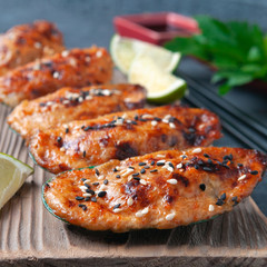Baked mussels with mozzarella cheese, spices and sesame seeds. On a wooden board. Decorated with lime slices. Close-up. In the background is lime, a bowl of soy sauce, chopsticks. Grey background.