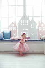 Fototapeta premium Portrait of a happy little blonde girl in a pink dress sitting on the windowsill