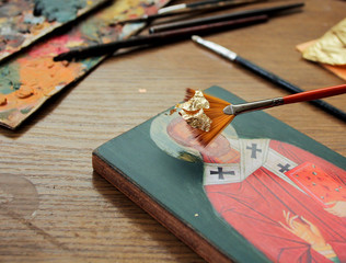 Hand with brush of gold leaf. Artist applies gold leaf to the icon. Reproduction of the icon of St....