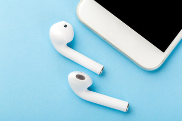Wireless bluetooth headphones with a modern mobile phone on a blue background.