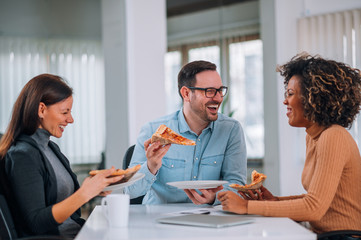 Laughing coworkers sharing pizza at workplace.