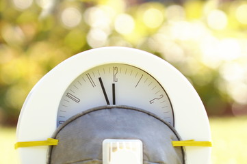 alarm clock in a protective respiratory mask on grass. Time to buy medical concept. White clock showing five minutes to 12, face mask on the light blurred garden background. coronavirus time Covid-19