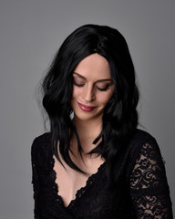 Close up portrait of a pretty, goth girl with dark hair  posing in front  a studio background.