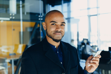 smiling young black designer creative man posing in workspace with mobile phone in his hands