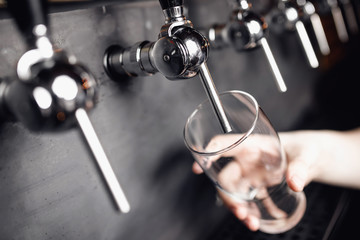 Bartender pours beer from tap into glass, dark background. Alcohol craft drink concept