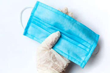 Hand in latex glove holding blue medical protective mask on white background. Coronavirus. Copy space