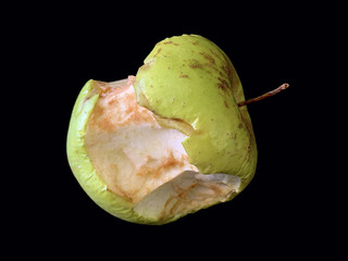 Nibbled green apple, on a black background. Old spoiled fruits, on a dark table. Perishable vitamins.