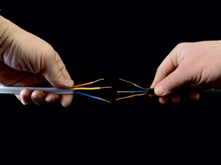 Open copper wires in a male hand. Electro wiring in hands, on a black background. Electrician