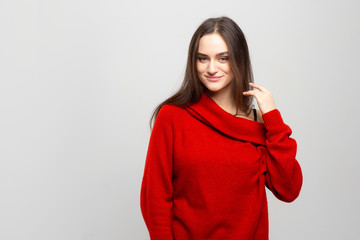 Fototapeta premium Portrait of a young beautiful woman with a light smile dressed in a red sweater on a light gray background.