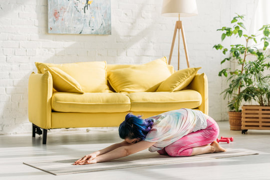 Girl with colorful hair in child pose on yoga mat in living room