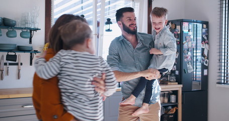 Happy young Caucasian mother and father playing with two little sons in the kitchen, family fun time at home slow motion