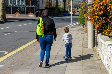 A mother walking alongside a small child riding a scooter