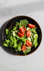 Summer fresh detox salad with tomatoes, cucumber, romaine lettuce and olive oil on marble background. Healthy diet food for vegan or vegetarian, top view