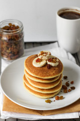 pancakes with banana on white plate and cup of coffee.  Breakfast in the kitchen