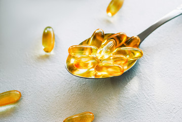Tablespoon holding omega 3 cod liver oil supplement capsules on a white table top with copy space
