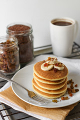 Delicious breakfast. Pancake with banana on a white plate. Containers with raisins and flax seeds