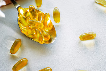 Tablespoon holding omega 3 cod liver oil supplement capsules on a white table top with copy space