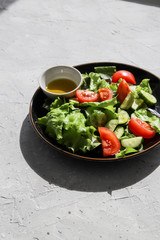 Summer fresh detox salad with tomatoes, cucumber, romaine lettuce and olive oil on grey concrete background. Healthy diet food for vegan or vegetarian