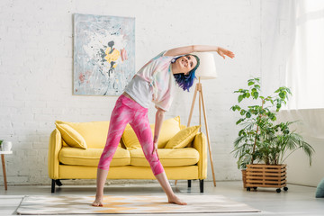 Girl with colorful hair warming up with outstretched hand and smiling in living room
