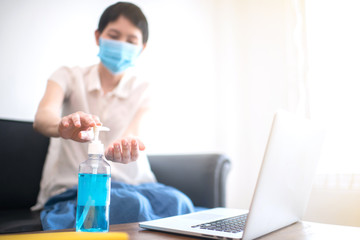 Sanitizer gel on table with blur  Asian business woman wearing surgical mask in background.Work from home with on line job during lock down quarantine period of pandemic corona virus or covid-19