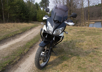 A black and white large motorcycle stands on a forest road. Nearby you can see the pond