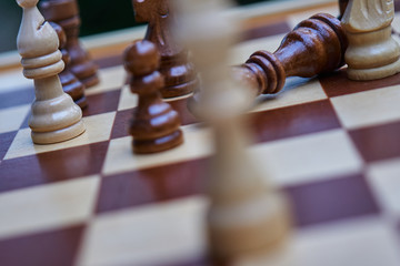 Intentionally crooked chessboard with blurred white king and toppled black king in the background,...