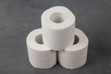 Pyramid of three toilet paper rolls on a gray background