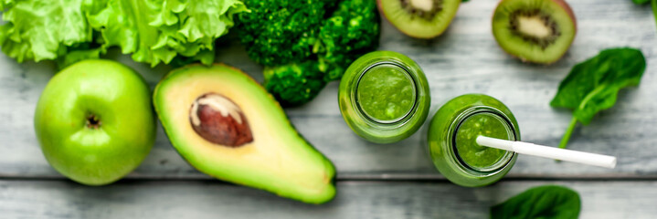  two green healthy smoothies made from apples, spinach, avocado, salad, kiwi on a wood background