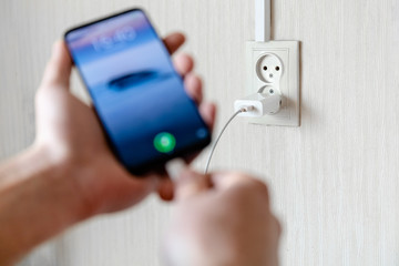blurred human hand turns on the smartphone to charge on the background of the outlet