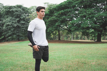 Young man runner stretching for warming up before running or working out in park.