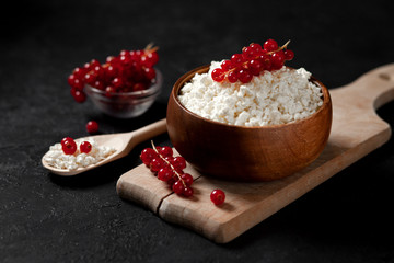 fresh home-made cottage cheese with currants in a wooden bowl against a dark background, healthy food with berries on a black table